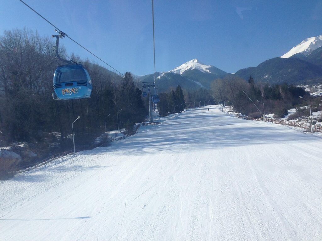 Cheap ski travel: Snow-covered ski slopes in Bansko, Bulgaria with mountains in the background.